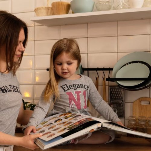 A mother and daughter enjoy reading a cookbook in a modern kitchen, sharing fun and learning together.