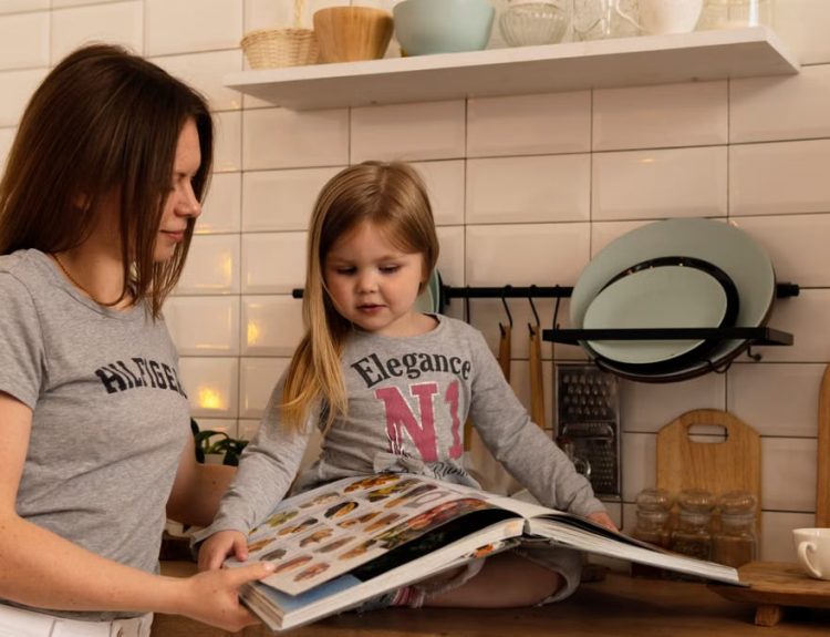 A mother and daughter enjoy reading a cookbook in a modern kitchen, sharing fun and learning together.
